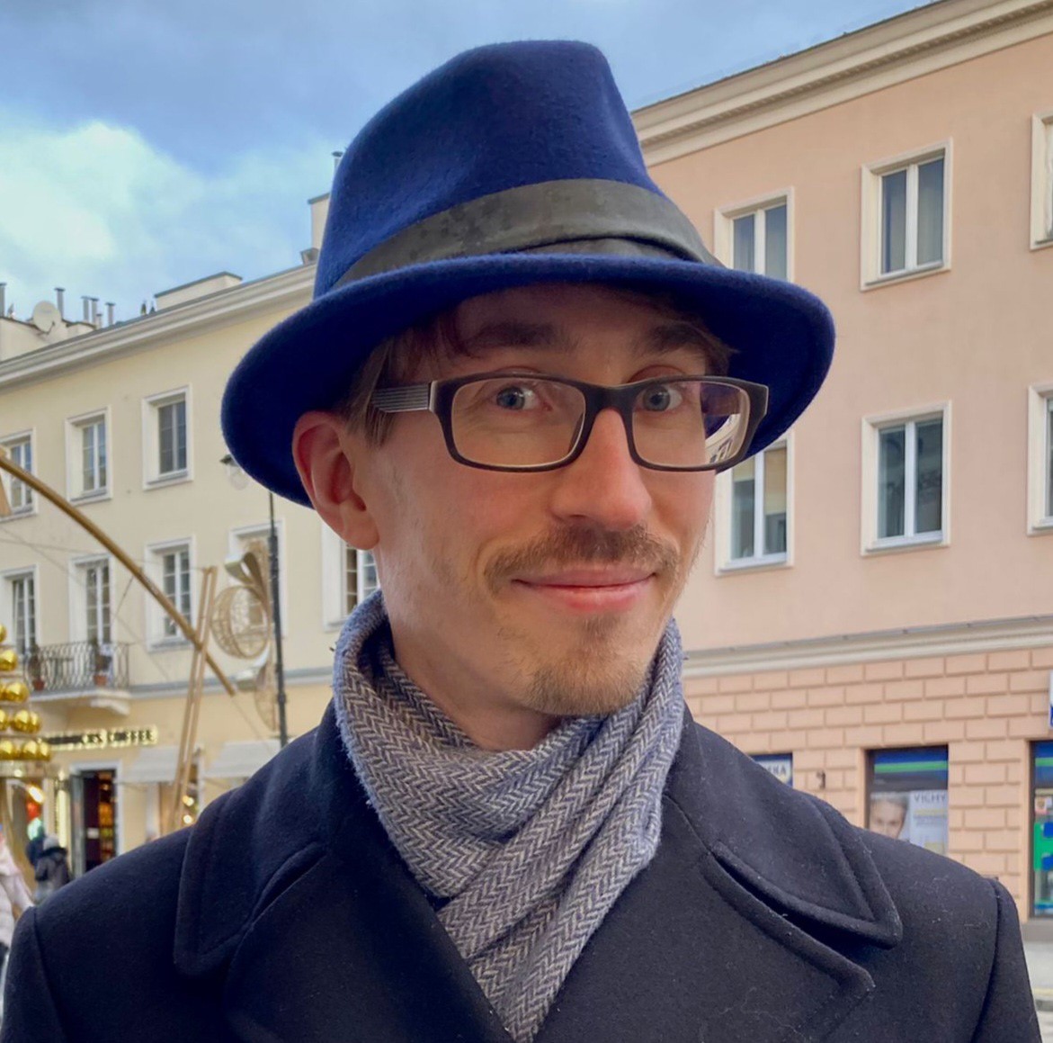 A smart young man in a bespoke blue fedora that goes as perfectly with his eyes as with his coat and his scarf.