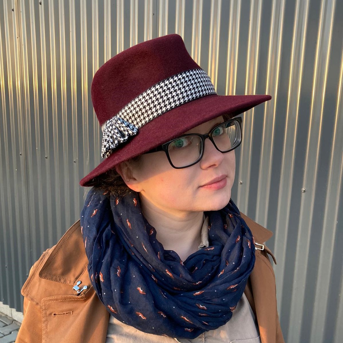 A woman wearing a bespoke burgundy hat with a black & white houndstooth ribbon. Add a trench and voila a perfect casual look.