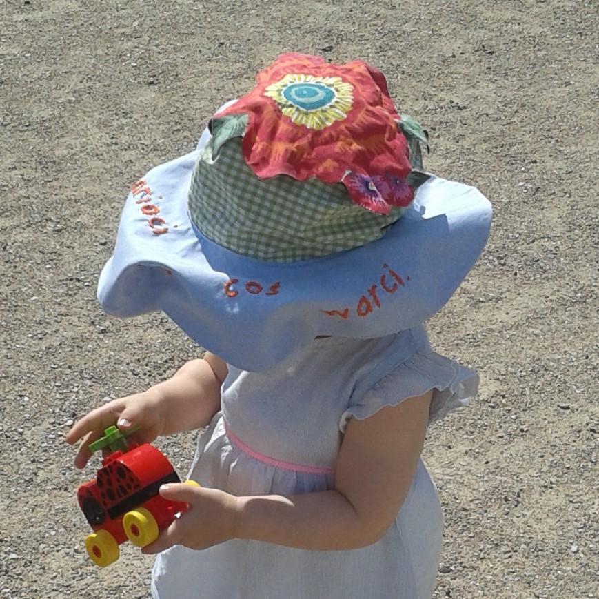 A baby girl in a custom-made reversible and adjustable baby hat with a flower on the crown and a brim that looks like a cloud