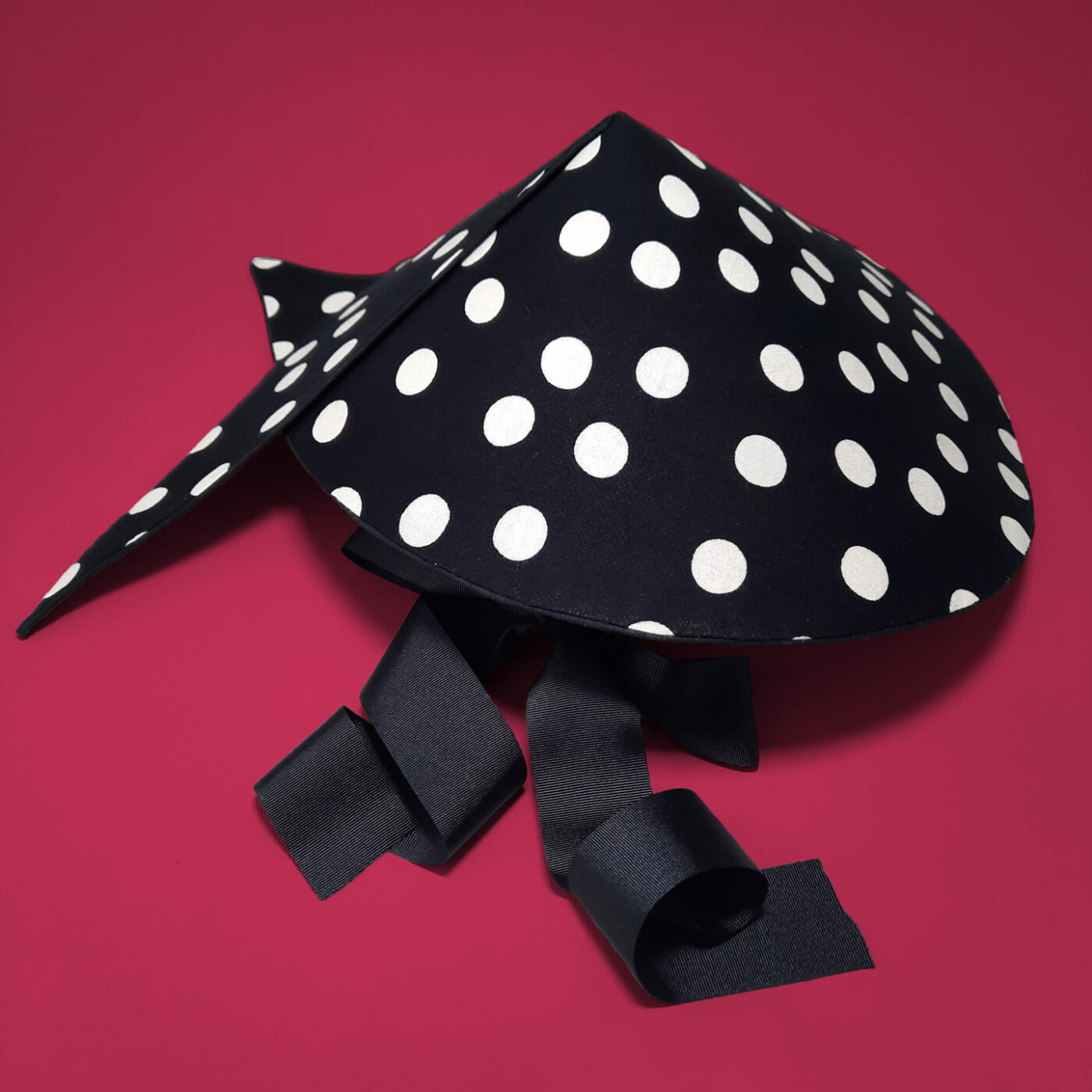 A summer hat with a polka dot black and white pattern. It's shape resembles a bit a chinese hat. It's a reversible hat.