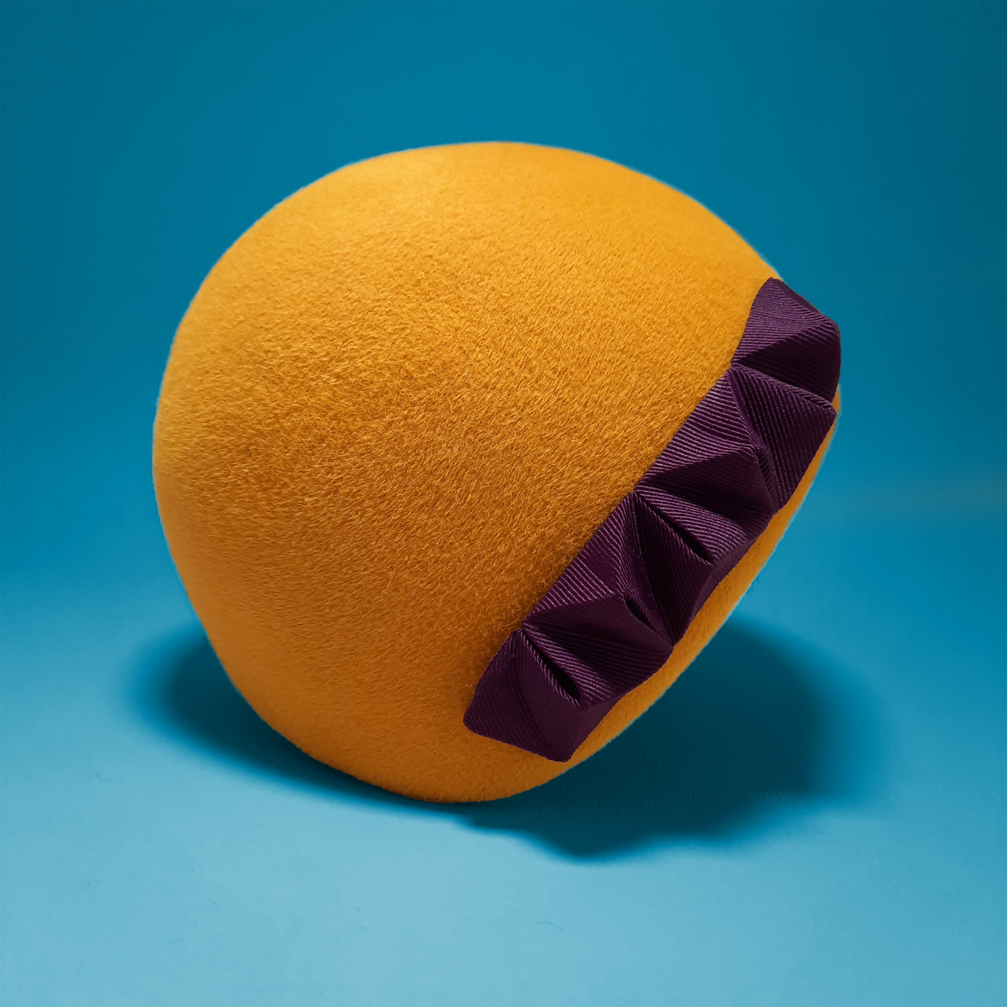 A yellow helmetlike fur felt hat with a purple 3D origami chameleon ornament which can be also worn as a bracelet.