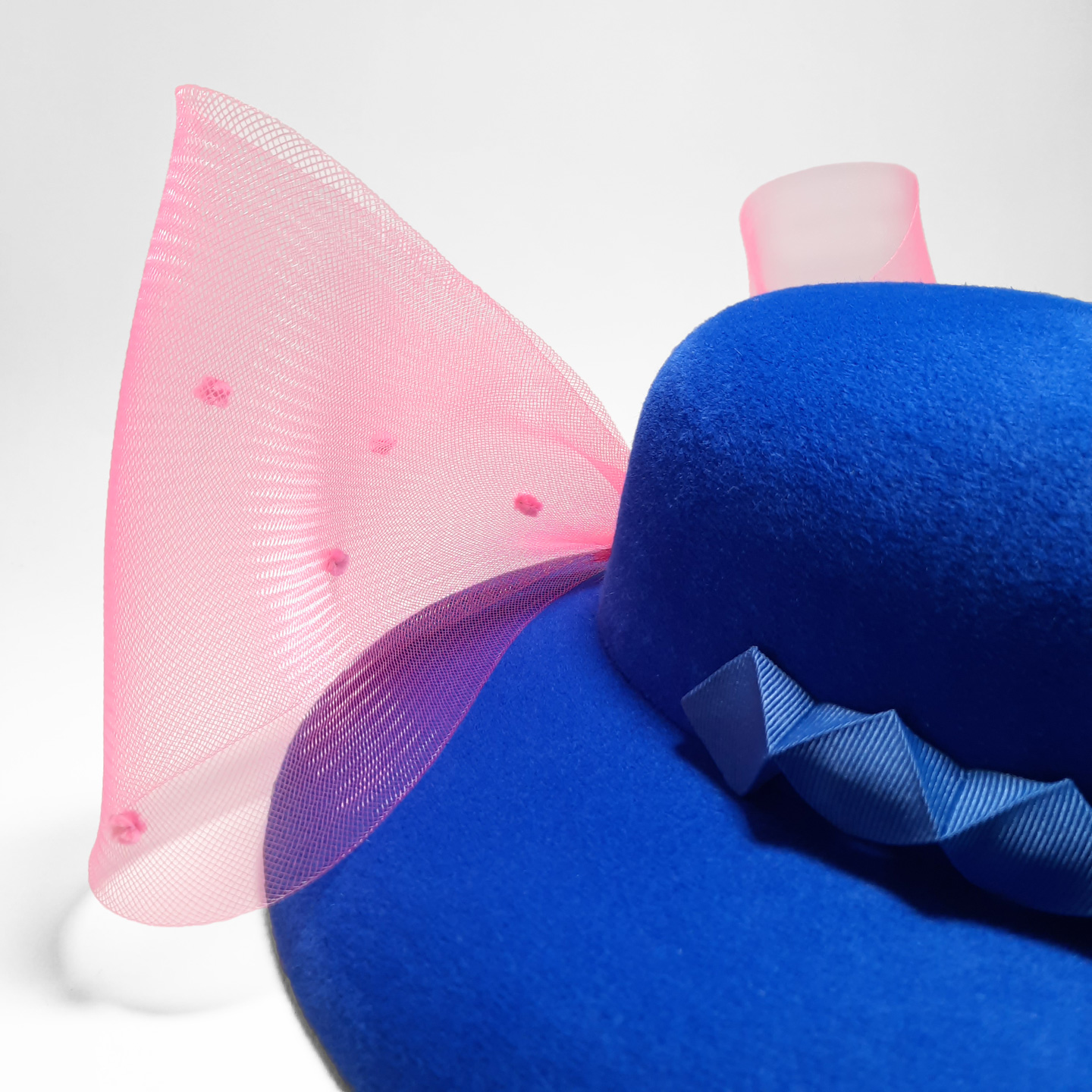 A luxury hat in a beautiful shade of cobalt blue. It's decorated with 3D chameleon detail and a detachable large pink bow.