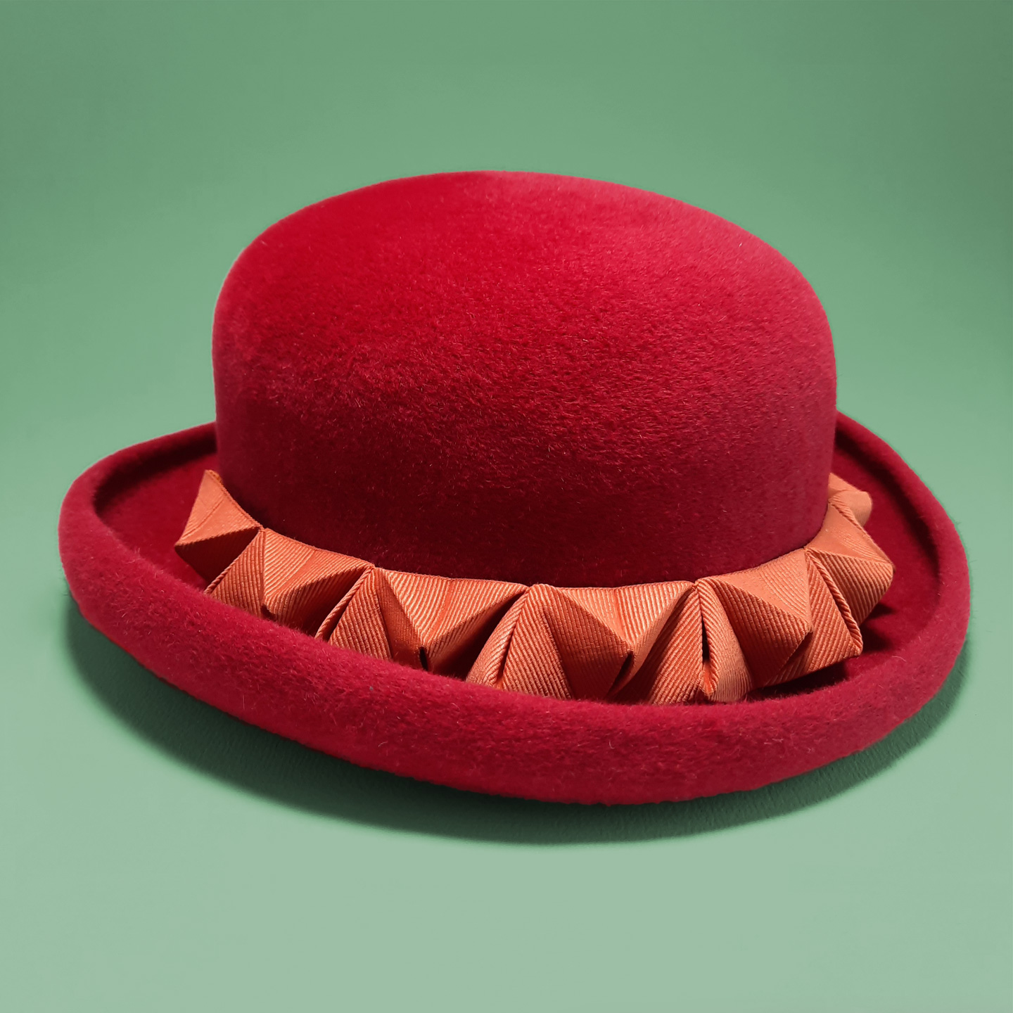 A red bowler hat with an orange 3D chameleon detail that can be transformed into a headband. A truly unique headpiece.