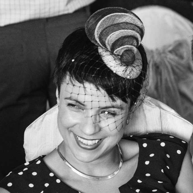 A smiling woman wearing a two-colour custom-made fascinator. Its pearled veil and her polka dot dress create a smart look. 