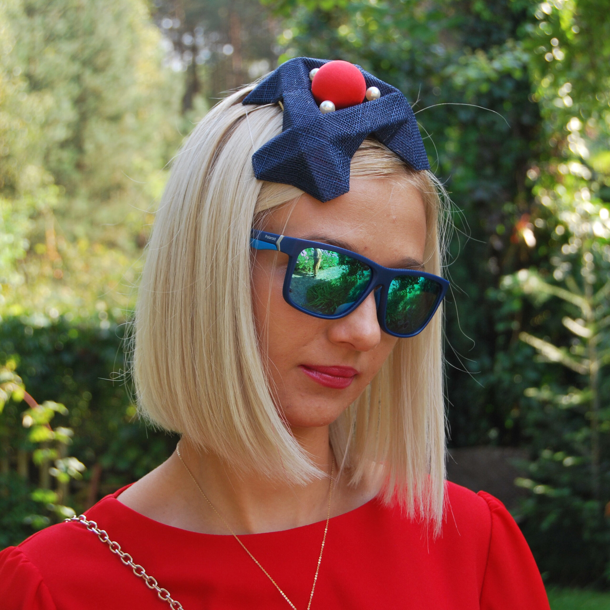 A very modern look combines a bespoke origami fascinator with a red dress, blue mirror shades and straight platine blond hair