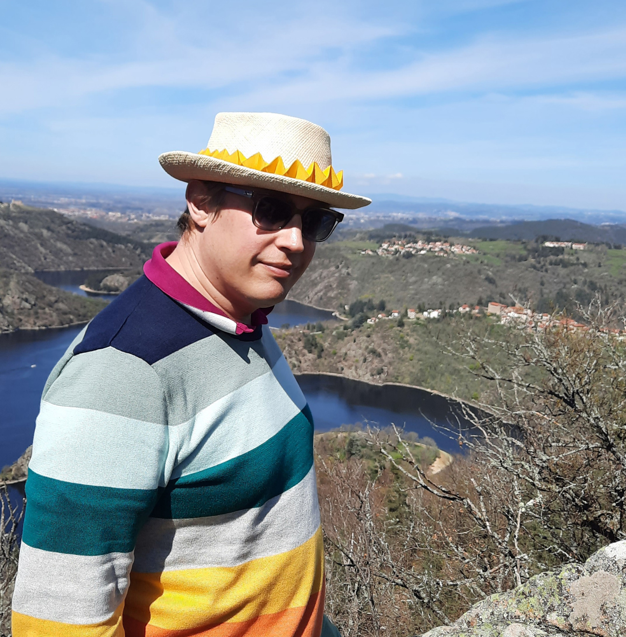 A man in a colorful sweater and a made to measure summer pork pie hat decorated with a striking yellow origami ornament.