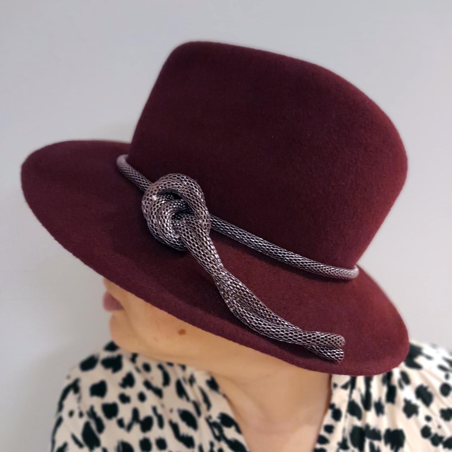 A woman a bespoke fedora. Her fur felt headpece is fitted with a silver chain tied in a knot for a modern & luxurious touch.