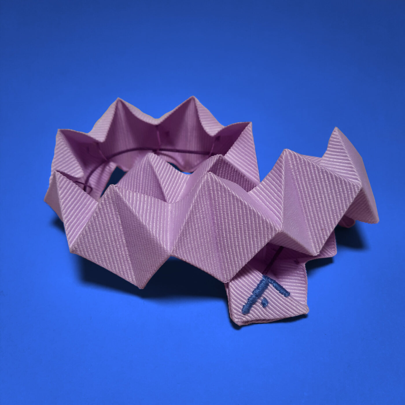 A lila pleated Fusanna hat ornament that can be used as a headband, or a necklace that's why it's called a chameleon detail.