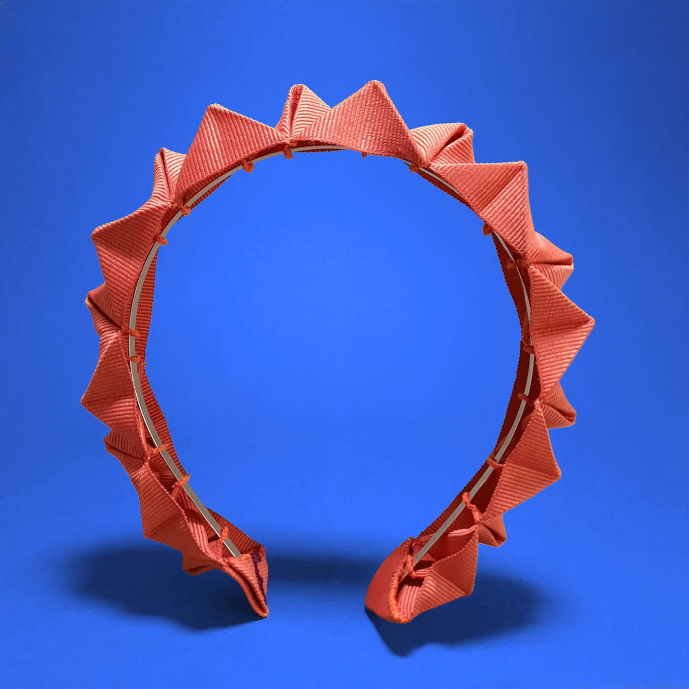 A brick orange headband made of petersham ribbon, neatly pleated and sewn by hand. It's a Fusanna signature chameleon detail.